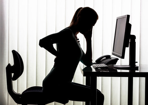 Silhouette of woman at desk having back pain