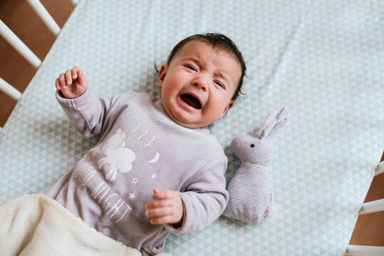 Portrait of crying baby girl lying in crib with toy bunny