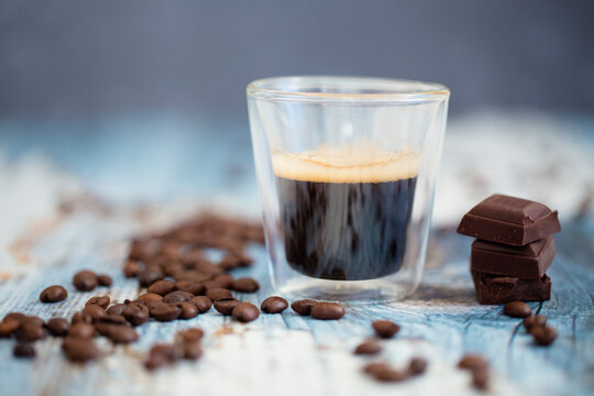 Glass cup of espresso, roasted coffee beans and dark chocolate on wood