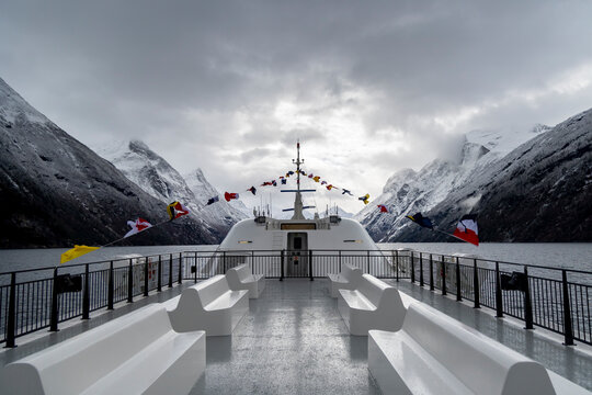 An empty upper deck of a tour ferry in fjords with nautical flags blowing in the wind. Winter scenery in Geirangerfjord, Sunnmore region, Norway.