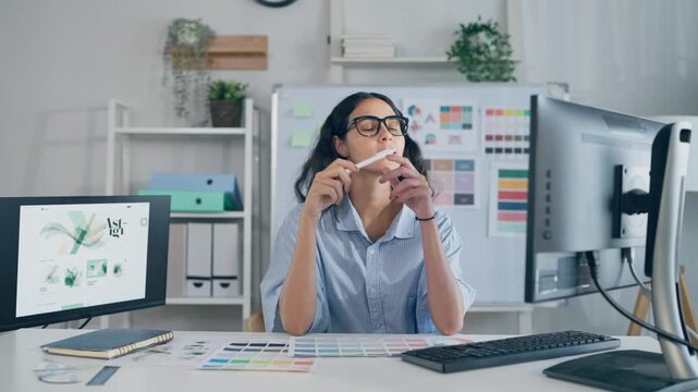 Young Hispanic woman designer sitting at her desk, working in an office.