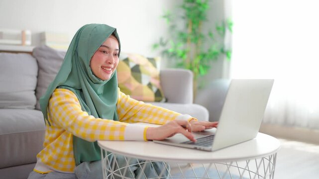 Asian Muslim woman student learning online class in living room at home. 