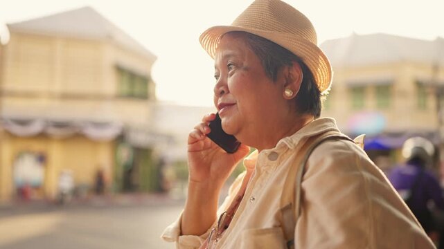 Asian senior woman talking on phone call while exploring city outdoors. 