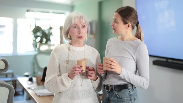 Two businesswomen drink coffee and discuss news during a break in the office. Coffee break. High quality 4k footage