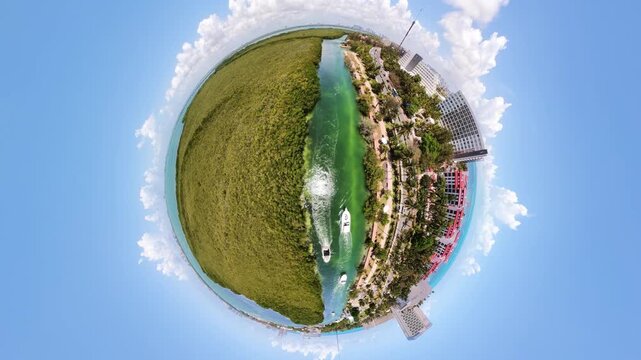 Stabilized 360 tiny planet drone shot over Laguna Nichupt&eacute; in Cancun, showing mangroves, turquoise water, bridge traffic, coastal buildings, sea, and sunny sky.