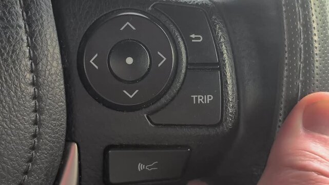 person sits in a car and uses their hand to press a trip button on the steering wheel.