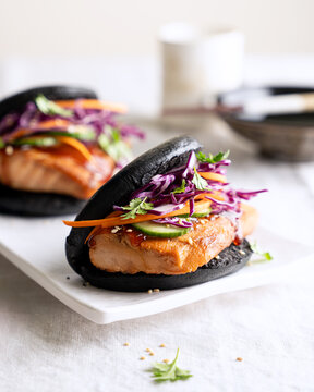 Close up of black salmon bao bun with purple cabbage slaw and sesame seeds