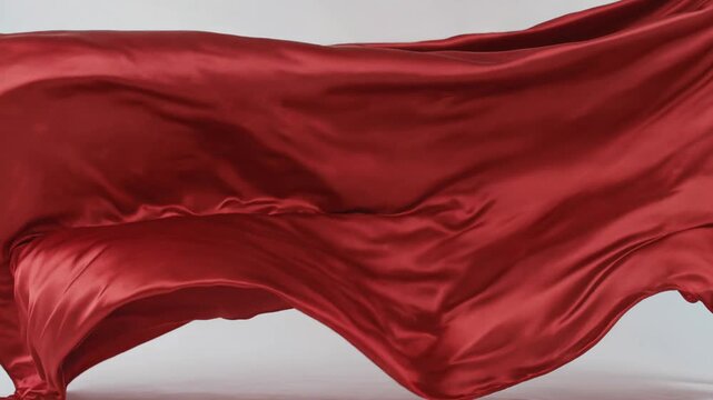 Elegant red silk fabric flowing in the wind against a plain background.