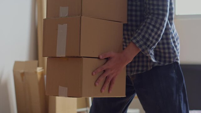 Young man struggles to lift and carry tall stack of three heavy cardboard moving boxes