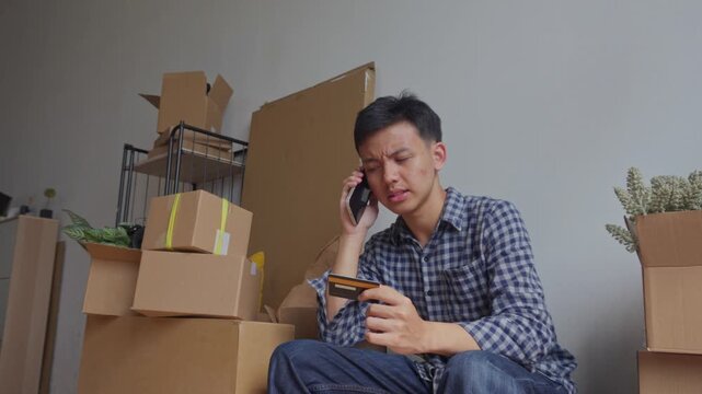 Frustrated man holds credit card and talks on his smartphone dealing with payment issue