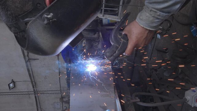 Close-up slow motion shot of a protected welder joining a circular metal piece with bright sparks and molten metal in a Cancun workshop.