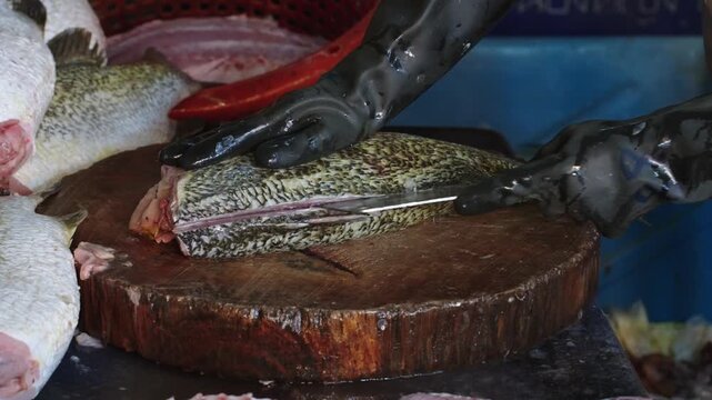 Close-up of a fishmonger cutting and filleting fresh fish on a wooden chopping block at a traditional seafood market. Raw seafood preparation process in an Asian wet market environment