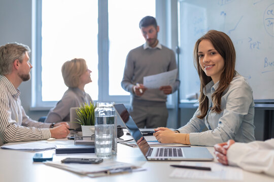Portrait of happy and successful business woman inside office at workplace, worker smiling and looking at camera with laptop, colleagues on the background