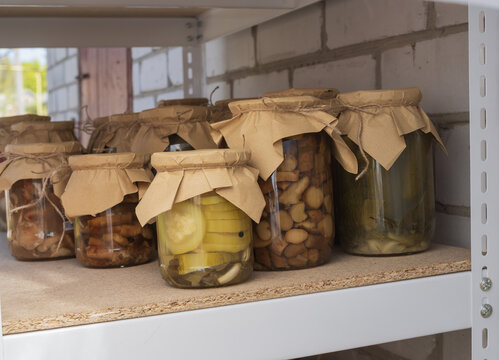 Collection of preserved vegetables, mushrooms, cucumbers, peppers, and tomato products in glass jars stored on shelves. Traditional home canning, food storage, and seasonal harvest preparation.
