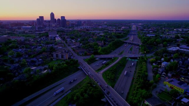 Aerial drone sunset over indianapolis city skyline with busy highway interchange traffic and suburban neighborhoods.