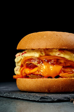 Gourmet vegetarian burger with melted cheddar cheese, sauce and pickles on black slate board, side view of delicious veggie cheeseburger on dark background, fast food delivery concept