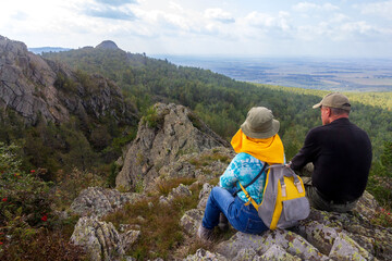 Fototapeta premium A beautiful elderly couple of tourists sits on the rocks and admires the beautiful views of the Ural Mountains