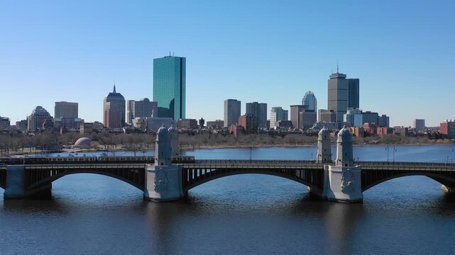 Red line train crossing Longfellow bridge with Boston skyline in background during bright sunny day over Charles river.
