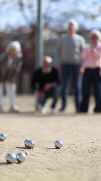 Team of senior people playing petanque, people play with small metal balls on sunny day on sports field. Positive people in jeans and shirts spend time outdoors while playing petanque