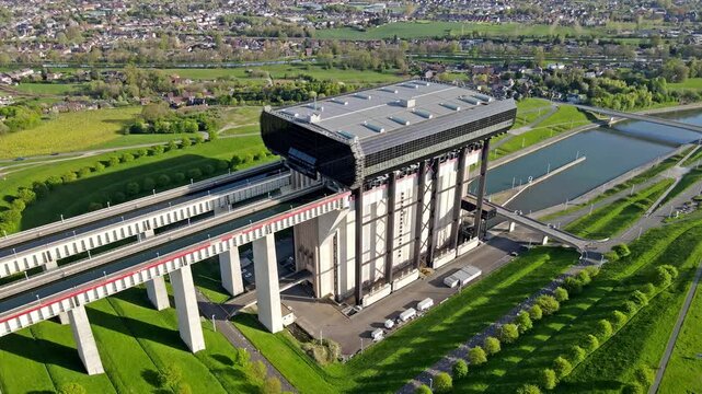 Aerial drone slow zoom-in on cargo barge entering canal lift chamber with steel gates and operator cabin visible. Calm water and loading sequence with industrial backdrop and bright spring day. Barge