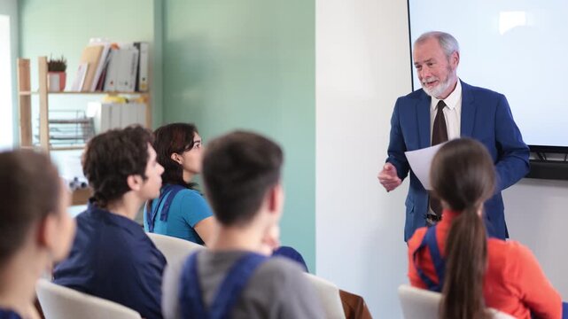 Mature male lecturer stands in front of young worker audience, delivers lecture. Safety briefing, introductory training for new employees, periodic training and professional development of employees