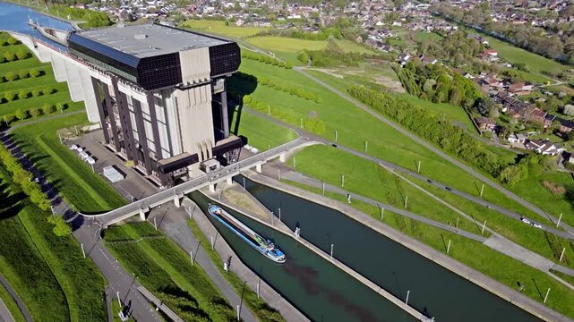 Static aerial drone view of cargo barge approaching and entering canal lift gates with docking procedures visible from above. Concrete tower and green landscape framing vessel entry into lift