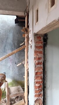 Construction worker vibrating fresh concrete to ensure compaction within the wooden formwork of a house pillar.