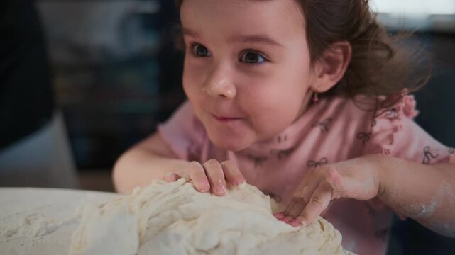 Young girl kneads dough with happy, focused expression. She wears pink shirt, flour dusts her hands. Perfect for cooking, family, or childhood activity themes