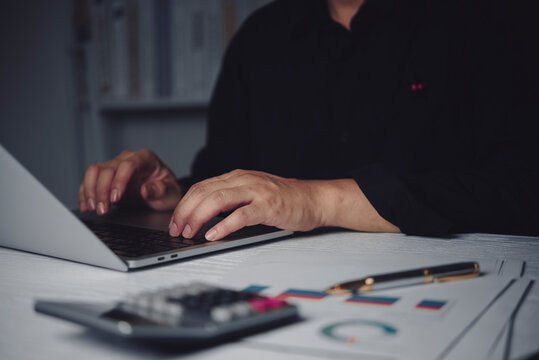 Accountant typing laptop keyboard analyzing financial graph chart calculator dark office late night overtime business investment tax audit corporate financial planning budget marketing strategy
