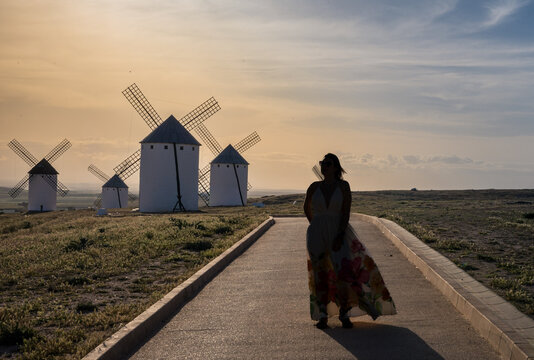 Woman walking toward historic windmills at sunset in Campo de Criptana, a famous destination in Castilla-La Mancha known for its connection to Don Quixote and Spanish cultural heritage.