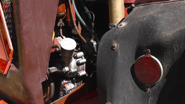 Close up view of an old red farm tractor's engine compartment and black fender with a circular reflector, showcasing details of the classic agricultural machinery on a sunny day