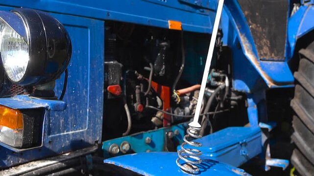 Close up view of a vintage blue agricultural tractor with its engine block visible, showcasing old round headlights, turn signals, and a large tire on a sunny day in the countryside