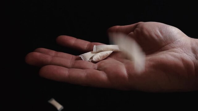 White smokeless nicotine pouches falling into a person's open palm against a black background. An alternative to smoking, these pouches are a popular way to consume nicotine without tobacco