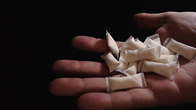 Close up of a person's hand holding a pile of modern white nicotine pouches, a tobacco free alternative to smoking and snus, presented in a studio setting with a dramatic black backtobacco alternative