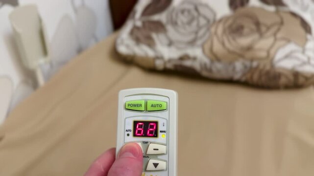 Close-up hand holding remote control adjusting heating temperature on massage bed, LED display changing digits, finger pressing