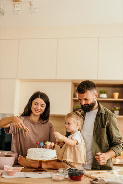 Happy family decorating a birthday cake together in the kitchen