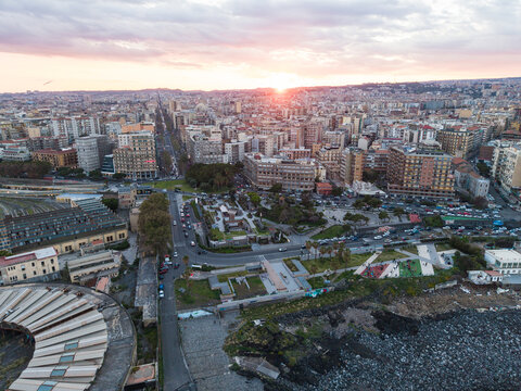 Aerial view of the urban cityscape at sunset with dense buildings and a rocky coastline in Catania, Sicily, Italy.