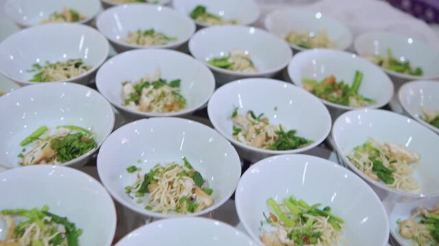 Rows of white soup bowls being meticulously prepared by catering staff on a long table