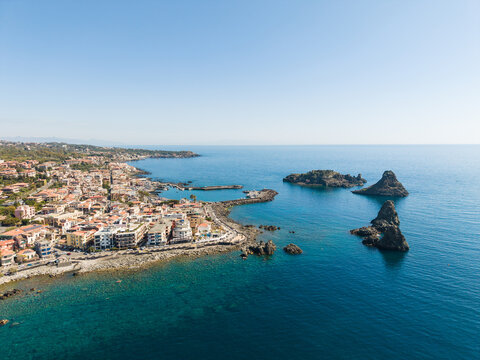 Aerial view of the Islands of the Cyclops and the coastal town of Aci Castello with volcanic rock formations and deep blue sea Aci Castello, Italy.