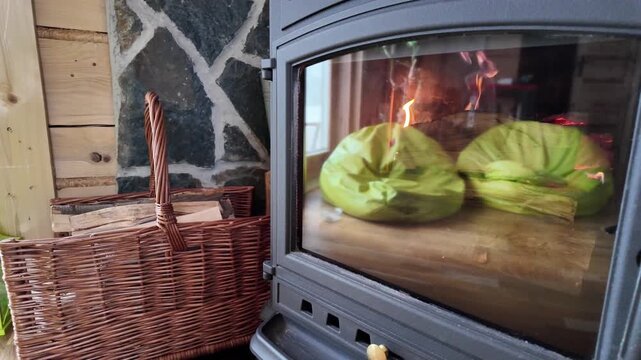 Close‑up of an anthracite cast iron stove with visible fires and cabin reflections, next to a wicker basket of kindling.