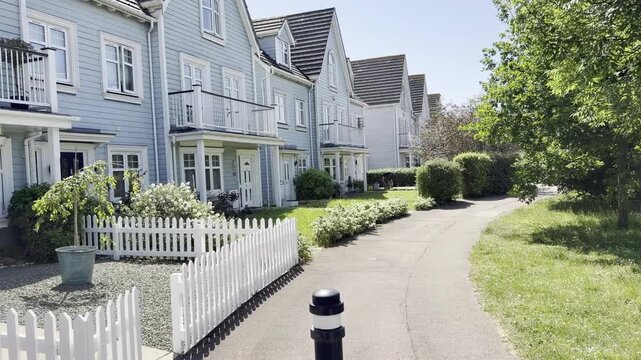 A row of light blue terraced houses with white picket fences and green gardens on a sunny day in Lee-On-The-Solent, England