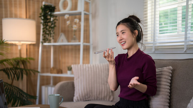 Asian woman using voice assistant smartphone technology hands free device speaking command message recording audio dictation app sitting home office living
