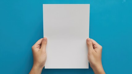 Obraz premium Hands holding a blank white sheet of paper on blue background
