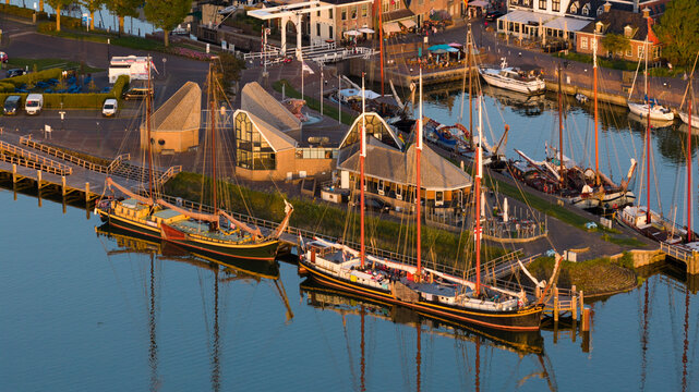 Aerial view of traditional sailing ships moored in the harbor with historic buildings and a drawbridge under golden hour light in Stavoren, Friesland, Netherlands.