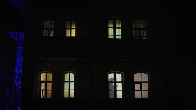 Silhouettes of people behind a window lit with warm orange light. A happy family in apartment windows, Music, violin, painting, reading books