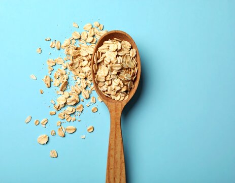 Natural Oat Flakes Spilled From Wooden Spoon on Bright Blue Background