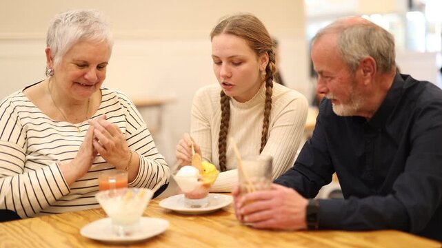 Teenage girl is talking with interest to her grandparents in a cafe, they ordered drinks with desserts. High quality 4k footage