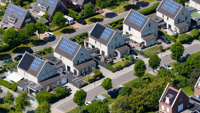 Aerial view of modern residential houses with solar panels on rooftops, lush green trees, and quiet suburban streets in Heerhugowaard, North Holland, Netherlands.