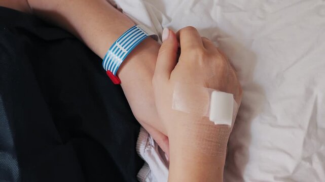 Recovering a patient who lies asleep in a hospital bed after surgery , hands on a blanket with information from the wristband. High quality 4k footage
