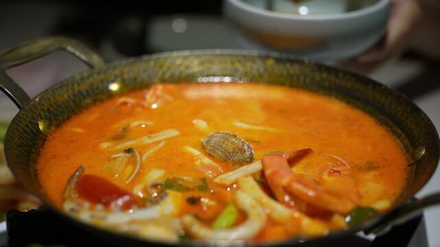 Close-up of authentic Thai Tom Yum Goong soup with shrimp, lemongrass, lime leaves, and chili, served in metal bowl, symbol of Thailands famous spicy and sour cuisine and Asian street food culture.